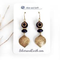 These handcrafted gold brass earrings have a contemporary modern style with an ethnic boho vibe. They feature brass drops with a lightly hammered texture accented with Tibetan eye agate gemstones, black glass and shiny brass beads. Bold and unique, they'll make a striking statement. Handmade in the USA by Silver and Earth Jewelry. 