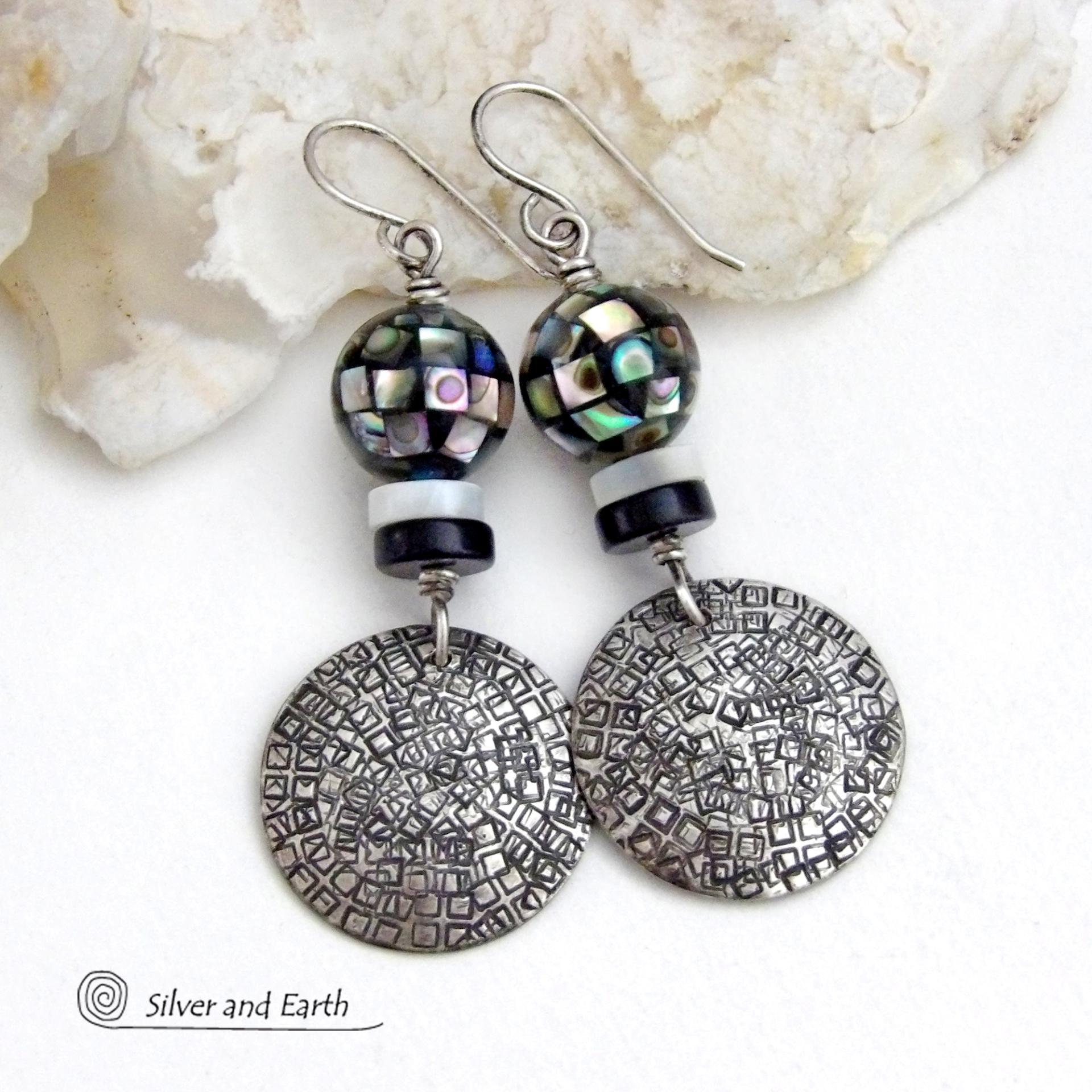 These handcrafted sterling silver earrings feature an abstract hand stamped texture and are accented with inlaid abalone shell mosaic, black onyx and mother-of-pearl beads. The abalone beads resemble disco balls and have a beautiful rainbow iridescence of various colors. Bold and unique, they have a modern contemporary style and will make a striking statement. Handmade in the USA by Silver and Earth Jewelry. Length: approx. 2-1/8” from top of sterling silver ear wires and 7/8". 