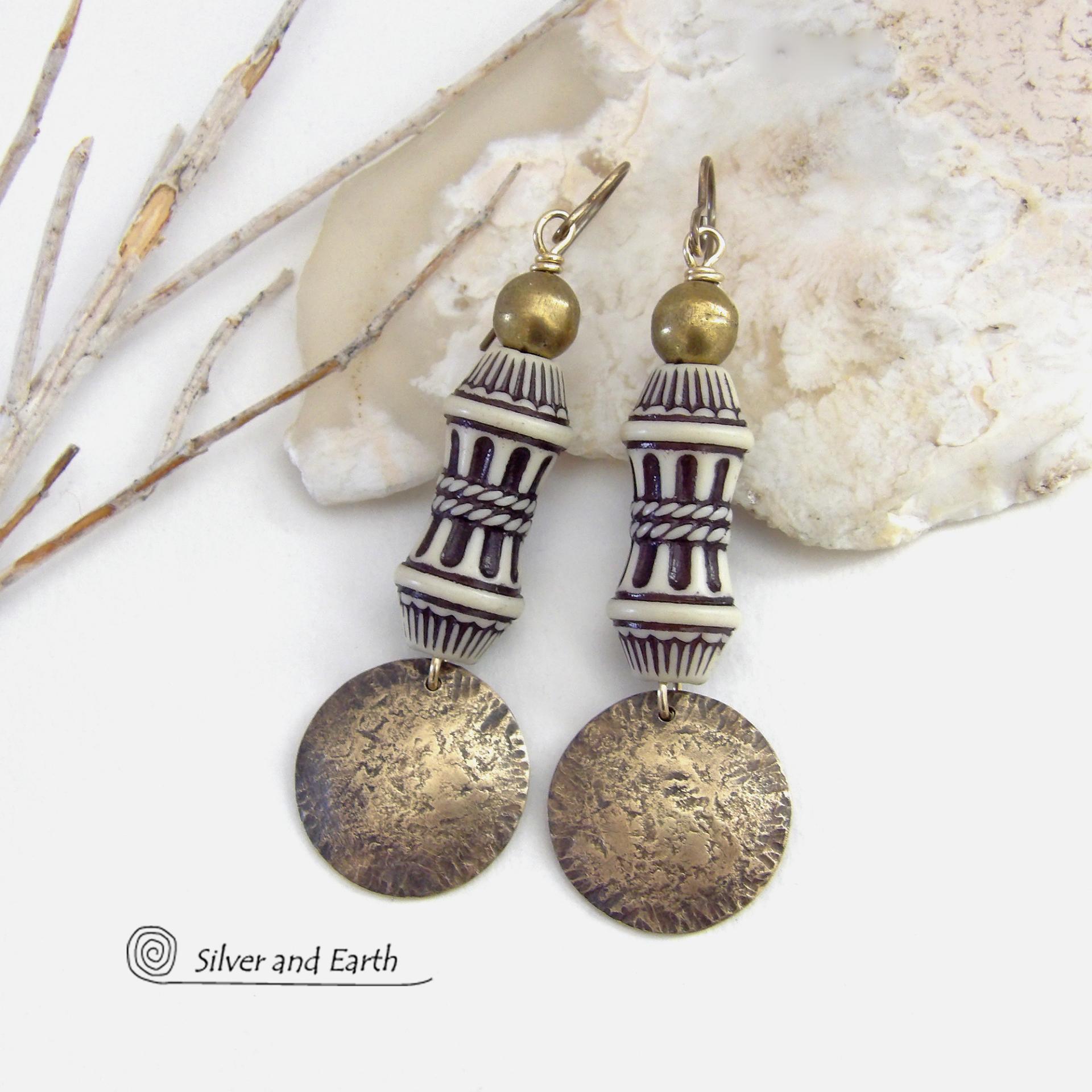 Bold and unique, these handcrafted earrings have an ethnic African tribal vibe. They feature gold brass dangles with a hammered rustic texture accented with exotic African beads with an intricate brown and white carved pattern topped off with gold brass beads. Unique and fun to wear - they'll make a bold, striking statement. Perfect for women that love to wear one-of-a-kind artisan handcrafted jewelry. Handmade in the USA by Silver and Earth Jewelry. 
