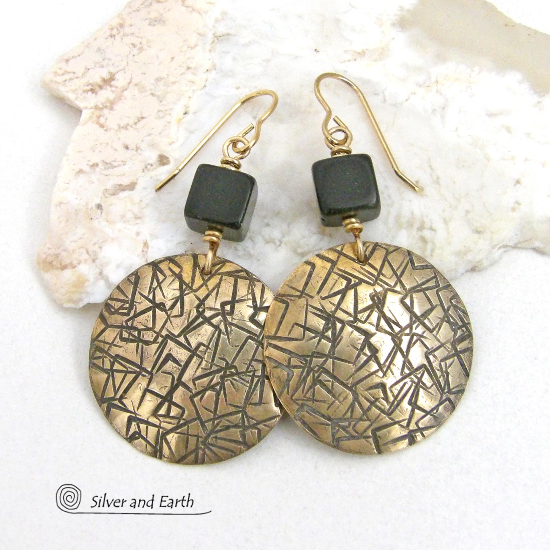 Artisan handcrafted round gold brass earrings with a hand-stamped abstract texture accented with cube-shaped matte black jasper stones on top. They have a modern contemporary vibe that coordinates beautifully with all wardrobe styles.