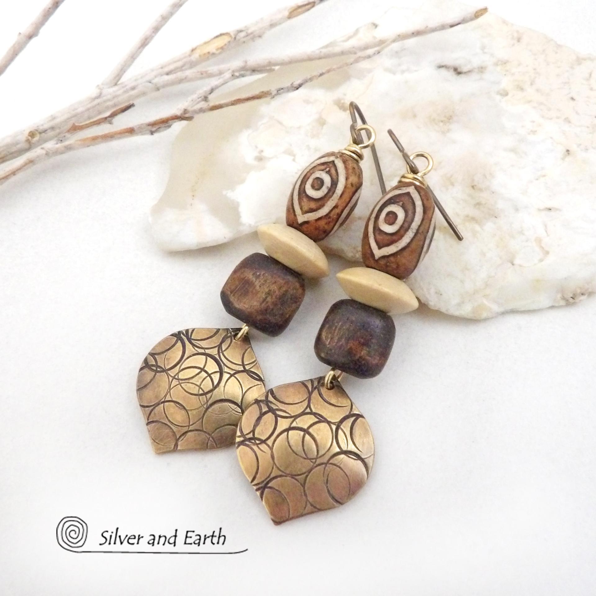 These handcrafted earrings feature gold brass dangles with a hand stamped texture accented with brown Tibetan etched agate stones, brown wood beads and tan wood saucer beads. Bold and unique, they have an ethnic tribal style with boho flair that makes a striking statement. Bold and striking, these handmade earrings are a beautiful example of bohemian-inspired jewelry.