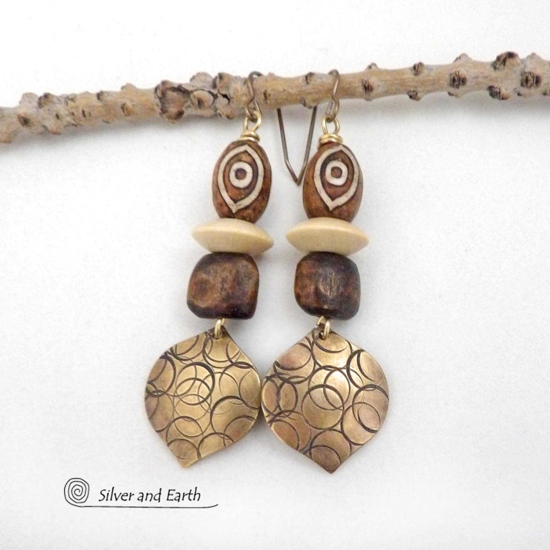 These handcrafted earrings feature gold brass dangles with a hand stamped texture accented with brown Tibetan etched agate stones, brown wood beads and tan wood saucer beads. Bold and unique, they have an ethnic tribal style with boho flair that makes a striking statement. Bold and striking, these handmade earrings are a beautiful example of bohemian-inspired jewelry.