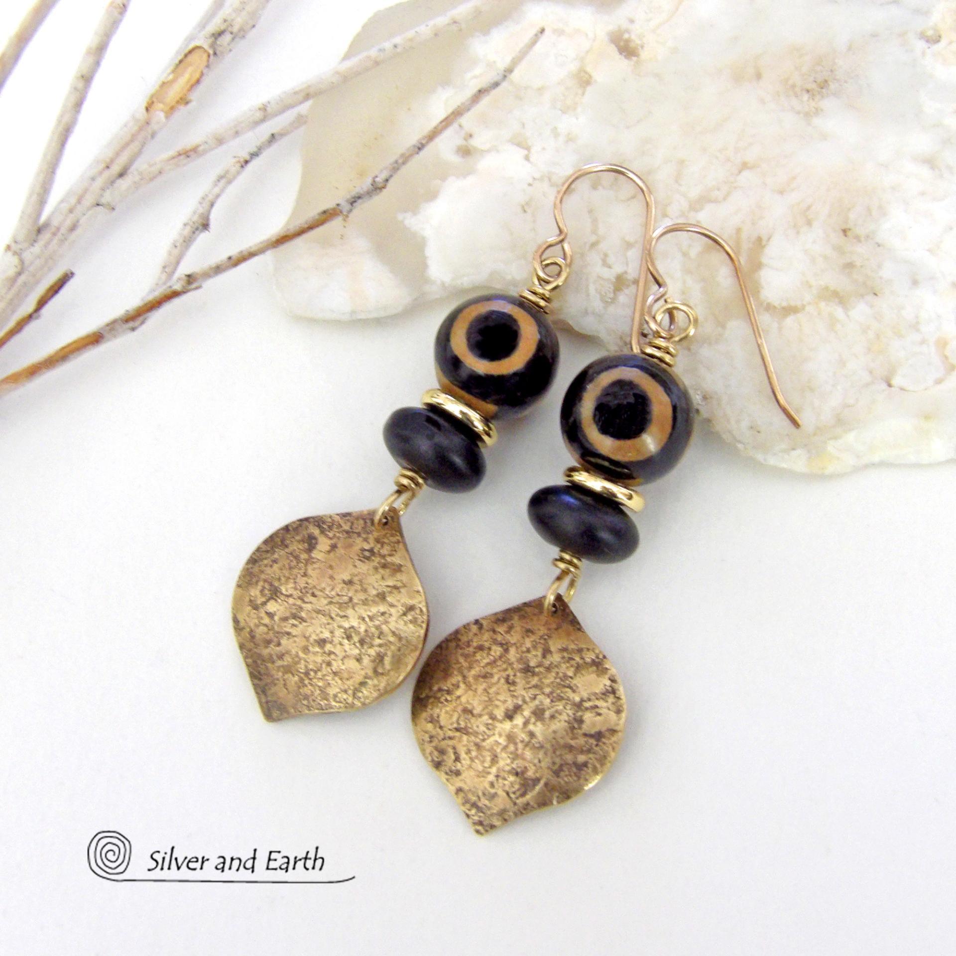 These handcrafted gold brass earrings have a contemporary modern style with an ethnic boho vibe. They feature brass drops with a lightly hammered texture accented with Tibetan eye agate gemstones, black glass and shiny brass beads. Bold and unique, they'll make a striking statement. Handmade in the USA by Silver and Earth Jewelry. 