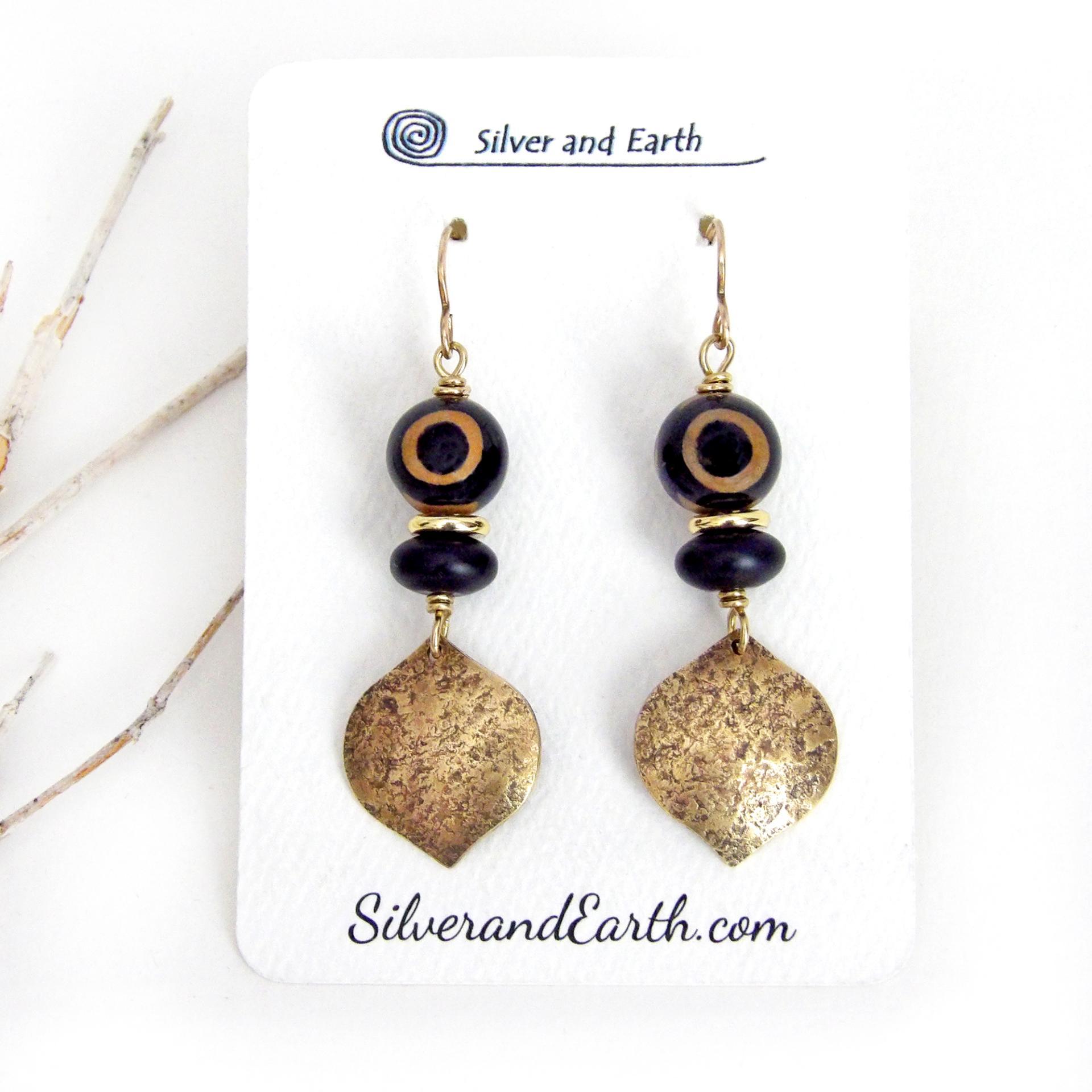These handcrafted gold brass earrings have a contemporary modern style with an ethnic boho vibe. They feature brass drops with a lightly hammered texture accented with Tibetan eye agate gemstones, black glass and shiny brass beads. Bold and unique, they'll make a striking statement. Handmade in the USA by Silver and Earth Jewelry. 