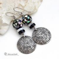 These handcrafted sterling silver earrings feature an abstract hand stamped texture and are accented with inlaid abalone shell mosaic, black onyx and mother-of-pearl beads. The abalone beads resemble disco balls and have a beautiful rainbow iridescence of various colors. Bold and unique, they have a modern contemporary style and will make a striking statement. Handmade in the USA by Silver and Earth Jewelry. Length: approx. 2-1/8” from top of sterling silver ear wires and 7/8". 