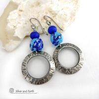 These handcrafted silver pewter hoop earrings have a hammered texture and feature blue African glass beads accented with bright blue glass beads. Vibrant and colorful, they'll add a touch of boho chic flair to your wardrobe. The African beads are handcrafted by artisans in Ghana from recycled glass by a traditional process passed down thru many generations. Handmade in the USA by Silver and Earth Jewelry. MEASUREMENTS: Total length: approximately 2-1/8" from top of silver niobium (hypoallergenic) ear wire