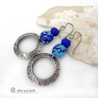 These handcrafted silver pewter hoop earrings have a hammered texture and feature blue African glass beads accented with bright blue glass beads. Vibrant and colorful, they'll add a touch of boho chic flair to your wardrobe. The African beads are handcrafted by artisans in Ghana from recycled glass by a traditional process passed down thru many generations. Handmade in the USA by Silver and Earth Jewelry. MEASUREMENTS: Total length: approximately 2-1/8" from top of silver niobium (hypoallergenic) ear wire