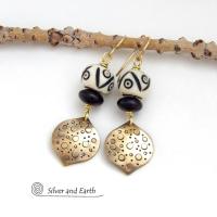 These handcrafted gold brass earrings have an ethnic, boho tribal vibe that makes a bold statement. They feature brass drops with a hand stamped texture accented with African carved bone beads with a bold pattern of dots and lines and matte black glass beads.