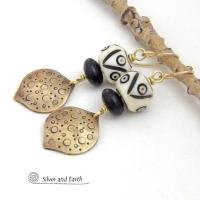 These handcrafted gold brass earrings have an ethnic, boho tribal vibe that makes a bold statement. They feature brass drops with a hand stamped texture accented with African carved bone beads with a bold pattern of dots and lines and matte black glass beads.