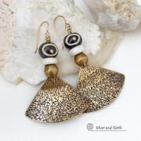 These handcrafted earrings feature gold brass fan-shaped dangles with a rustic hammered texture accented with African batik bone beads, off-white magnesite stones and African brass beads. Unique and striking, they have a bold ethnic vibe with African tribal flair that makes a striking statement. Handmade in the USA by Silver and Earth Jewelry. 