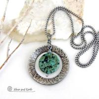 This handcrafted pendant necklace features a natural coin-shaped African turquoise gemstone framed against a hammered and oxidized silver tone pewter circle. It has a modern earthy organic style that coordinates well with all wardrobe types. The design is versatile and can be worn by either a man or woman. It will make a great gift for anyone that loves natural stone jewelry. Handmade in the USA by Silver and Earth Jewelry. 