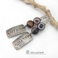 These handcrafted sterling silver earrings feature sterling silver rectangles with a hammered and hand stamped texture accented with natural Botswana agate gemstones. The stones have a smoky brown hue with a natural orbicular "eye" and line pattern. Botswana agate is a unique, banded chalcedony from Southern Africa. Bold and unique, these earrings are one-of-a-kind and will make a striking statement.