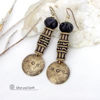 Bold and unique, these handcrafted earrings have an ethnic African tribal vibe. They feature gold brass dangles with a hand stamped and lightly hammered background texture accented with African beads with an intricately carved brownish-black and tan pattern topped off with black African carved bone beads. Unique and fun to wear - they'll make a bold, striking statement. Perfect for women that love to wear one-of-a-kind artisan handcrafted jewelry. Handmade in the USA by Silver and Earth Jewelry.