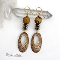 These handcrafted earrings feature gold brass oval hoop dangles with a hand stamped texture accented with natural brown tiger's eye gemstones and faceted hematite stones with an electroplated champagne gold finish. The stones have a beautiful brown hue with undertones of gold and a faceted finish which casts off a natural sparkle and shine. They have a modern, chic and elegant style that coordinates beautifully with all wardrobe types - dressed up or down.