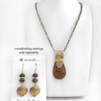This handcrafted necklace features a natural bronzite gemstone accented with a gold brass bail. The stone has a beautiful chocolate brown hue with a subtle golden shimmer. Bronzite is a mineral that shares characteristics with rock that is found in meteorites, such as iron. It's this blend of several minerals which gives bronzite its unique mottled characteristic. The necklace has an earthy, modern style that coordinates beautifully with all wardrobe types. 