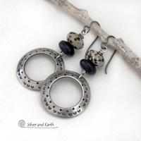 These handcrafted silver pewter hoop earrings have a hand stamped texture accented with natural dalmatian jasper gemstones and matte black glass beads. This type of jasper is known for its spotted pattern that resembles the Dalmatian breed of dog. These earrings have a modern, earthy boho chic style that coordinates beautifully with all wardrobe styles. Handmade the USA by Silver and Earth Jewelry.