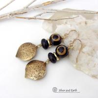 These handcrafted gold brass earrings have a contemporary modern style with an ethnic boho vibe. They feature brass drops with a lightly hammered texture accented with Tibetan eye agate gemstones, black glass and shiny brass beads. Bold and unique, they'll make a striking statement. Handmade in the USA by Silver and Earth Jewelry. 