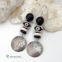 These earrings have a modern style with an ethnic tribal vibe. They feature handcrafted sterling silver circle dangles with a hammered texture accented with black and white Tibetan eye agate gemstones, onyx and bone beads, topped off with round black onyx gemstones with a faceted finish. Unique and striking, they'll make a bold statement. 