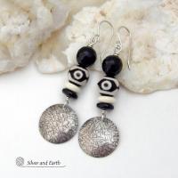 These earrings have a modern style with an ethnic tribal vibe. They feature handcrafted sterling silver circle dangles with a hammered texture accented with black and white Tibetan eye agate gemstones, onyx and bone beads, topped off with round black onyx gemstones with a faceted finish. Unique and striking, they'll make a bold statement. 