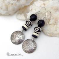 These earrings have a modern style with an ethnic tribal vibe. They feature handcrafted sterling silver circle dangles with a hammered texture accented with black and white Tibetan eye agate gemstones, onyx and bone beads, topped off with round black onyx gemstones with a faceted finish. Unique and striking, they'll make a bold statement. 