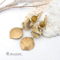Unique and one-of-a-kind, these artisan handcrafted earrings feature shiny gold brass dangles with a hammered raw silk texture accented with graphic feldspar and golden tiger's eye gemstones and shiny brass beads. Graphic feldspar is a type of moonstone that has smoky quartz inclusions which creates unique natural patterns. They have an elegant, modern chic style that looks great dressed up or down. 