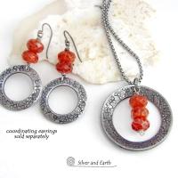 This handcrafted pendant necklace features a silver tone pewter circle with a hand stamped texture accented with a stack of faceted orange fire agate gemstones that dangle in front. It has a classic, earthy modern style that coordinates well with all wardrobe types. Matching earrings sold separately.
