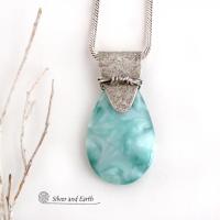 A stunning, natural green moonstone is accented with a handcrafted sterling silver bail in this one-of-a-kind pendant necklace. The stone has a beautiful mint green hue with a creamy white matrix. The bail is accented with twists of oxidized sterling silver wire. Bold and unique, it's sure to make a striking statement. 