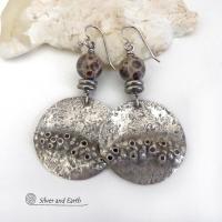 Unique and one-of-a-kind, these handcrafted large sterling silver earrings have a bold edgy vibe. They feature rustic hammered sterling silver accented with natural asteroid jasper stones and stainless steel beads. This type of stone is known for its unique dotted matrix in earth-tone hues of brown, gray and tan. It's also known as chocolate ocean jasper because it's found on the shores of Madagascar where ocean jasper is also found. Bold and exotic - they're sure to make a unique statement.