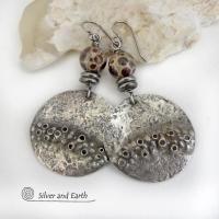 Unique and one-of-a-kind, these handcrafted large sterling silver earrings have a bold edgy vibe. They feature rustic hammered sterling silver accented with natural asteroid jasper stones and stainless steel beads. This type of stone is known for its unique dotted matrix in earth-tone hues of brown, gray and tan. It's also known as chocolate ocean jasper because it's found on the shores of Madagascar where ocean jasper is also found. Bold and striking - they're sure to make a unique statement.
