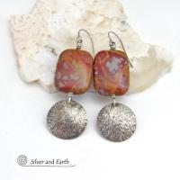 These one-of-a-kind handcrafted earrings feature natural Noreena jasper gemstones accented with textured sterling silver dangles. This stone is known for its dramatic abstract and geometric patterns and is found only in the Pilbara region of Western Australia. The stones in this pair have a great pattern consisting of hues of deep burgundy-red with fiery orange and gray streaks. 