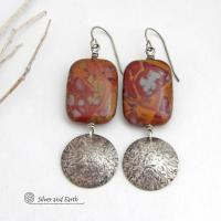 These one-of-a-kind handcrafted earrings feature natural Noreena jasper gemstones accented with textured sterling silver dangles. This stone is known for its dramatic abstract and geometric patterns and is found only in the Pilbara region of Western Australia. The stones in this pair have a great pattern consisting of hues of deep burgundy-red with fiery orange and gray streaks. 