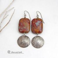 These one-of-a-kind handcrafted earrings feature natural Noreena jasper gemstones accented with textured sterling silver dangles. This stone is known for its dramatic abstract and geometric patterns and is found only in the Pilbara region of Western Australia. The stones in this pair have a great pattern consisting of hues of deep burgundy-red with fiery orange and gray streaks. 