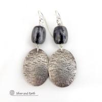 These handcrafted earrings feature sterling silver oval dangles accented with Picasso marble gemstones. This semiprecious stone is found only in southwest Utah. It's named after the famous artist because the natural matrix of geometric lines resembles an abstract painting. The stones in this pair have distinctive swirly lines in black and grey. They have a modern, earthy style and are lightweight and comfortable to wear.
