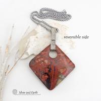 This artisan handcrafted one-of-a-kind necklace features a natural red creek jasper stone accented with a hand forged sterling silver bail with a lightly hammered texture. The stone has a beautiful natural pattern in earthy hues of mossy greens, brick red, brown and orange. It's reversible and can be worn on either side. (See all photos for alternate sides). It makes a great gift for anyone that loves earthy colors and natural stones. The design is unisex so it could be worn by a man or woman.
