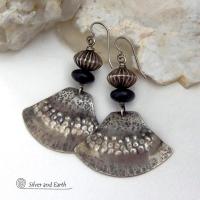 These handcrafted sterling silver earrings have a modern southwestern flair. The sterling shapes have a hammered and stamped texture with an oxidized finish. They are accented with Native Navajo pearl style oxidized sterling silver beads with a rich, corrugated texture and matte black glass beads. Unique and striking, they'll make a bold statement. Handmade in the USA by Silver and Earth Jewelry.