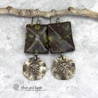 Large chunky spotted jasper stones are accented with handcrafted rustic sterling silver dangles in these one-of-a-kind earrings. The silver has an earthy hammered organic texture with a few holes for a primal effect. The stones have a dark brownish-black base with a natural matrix of green spots and a faceted finish.
