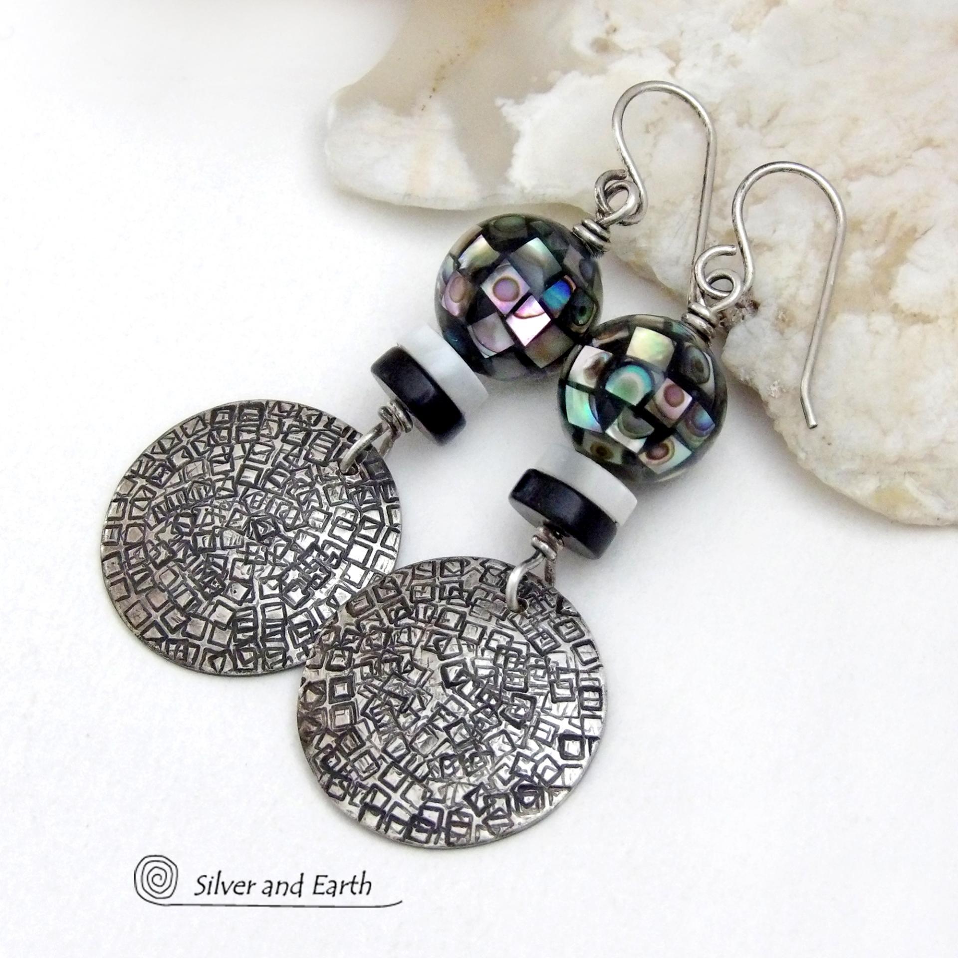 These handcrafted sterling silver earrings feature an abstract hand stamped texture and are accented with inlaid abalone shell mosaic, black onyx and mother-of-pearl beads. The abalone beads resemble disco balls and have a beautiful rainbow iridescence of various colors. Bold and unique, they have a modern contemporary style and will make a striking statement. Handmade in the USA by Silver and Earth Jewelry. Length: approx. 2-1/8” from top of sterling silver ear wires and 7/8". 