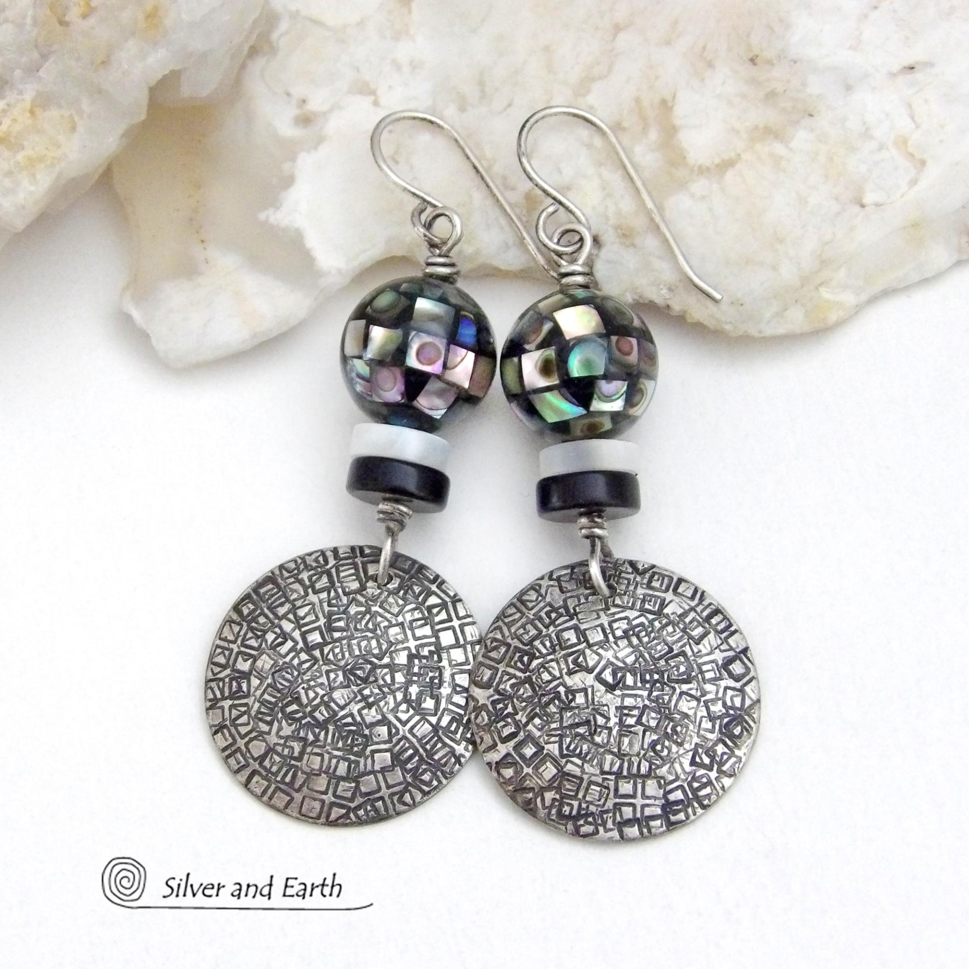 These handcrafted sterling silver earrings feature an abstract hand stamped texture and are accented with inlaid abalone shell mosaic, black onyx and mother-of-pearl beads. The abalone beads resemble disco balls and have a beautiful rainbow iridescence of various colors. Bold and unique, they have a modern contemporary style and will make a striking statement. Handmade in the USA by Silver and Earth Jewelry. Length: approx. 2-1/8” from top of sterling silver ear wires and 7/8". 