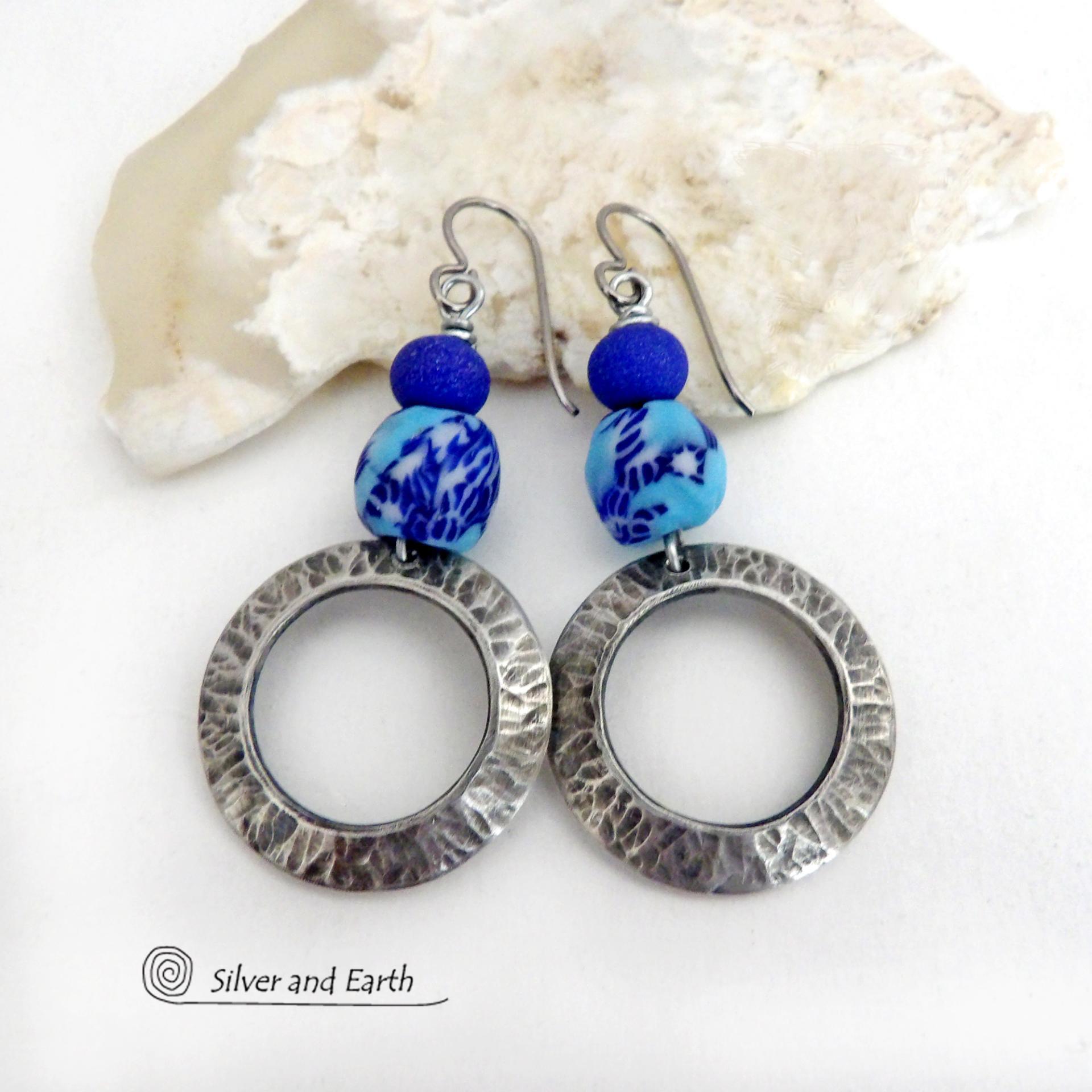 These handcrafted silver pewter hoop earrings have a hammered texture and feature blue African glass beads accented with bright blue glass beads. Vibrant and colorful, they'll add a touch of boho chic flair to your wardrobe. The African beads are handcrafted by artisans in Ghana from recycled glass by a traditional process passed down thru many generations. Handmade in the USA by Silver and Earth Jewelry. MEASUREMENTS: Total length: approximately 2-1/8" from top of silver niobium (hypoallergenic) ear wire