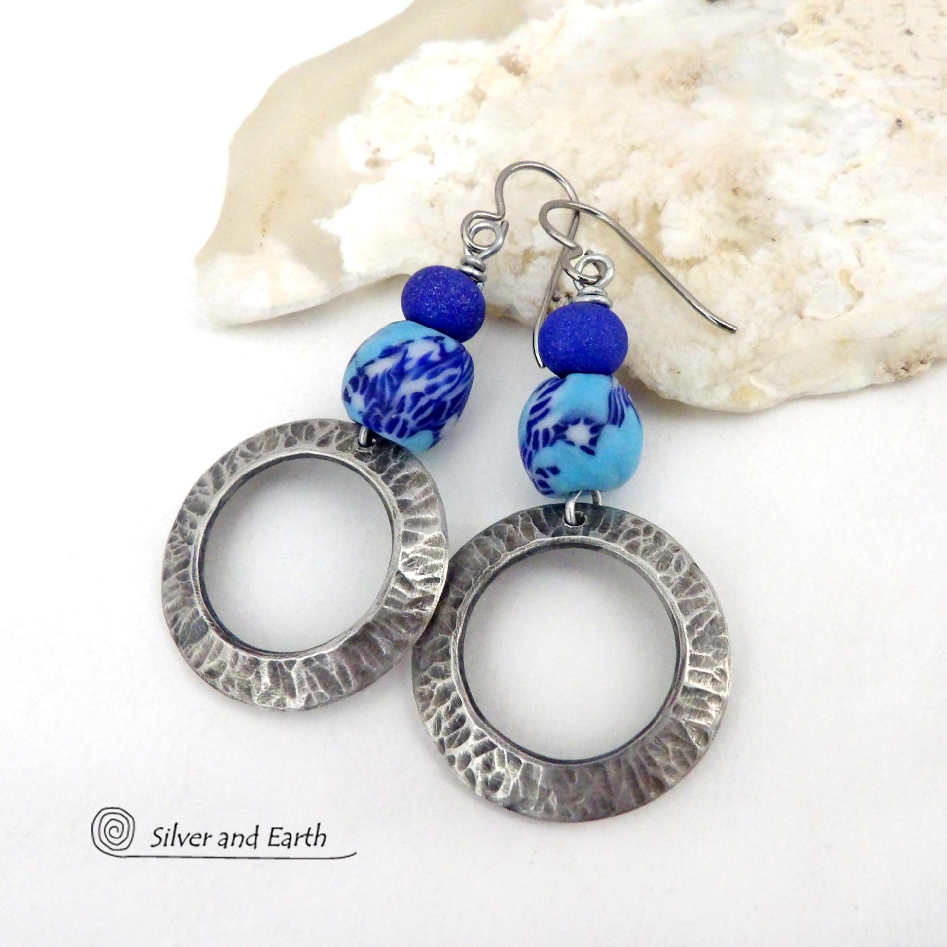 These handcrafted silver pewter hoop earrings have a hammered texture and feature blue African glass beads accented with bright blue glass beads. Vibrant and colorful, they'll add a touch of boho chic flair to your wardrobe. The African beads are handcrafted by artisans in Ghana from recycled glass by a traditional process passed down thru many generations. Handmade in the USA by Silver and Earth Jewelry. MEASUREMENTS: Total length: approximately 2-1/8" from top of silver niobium (hypoallergenic) ear wire