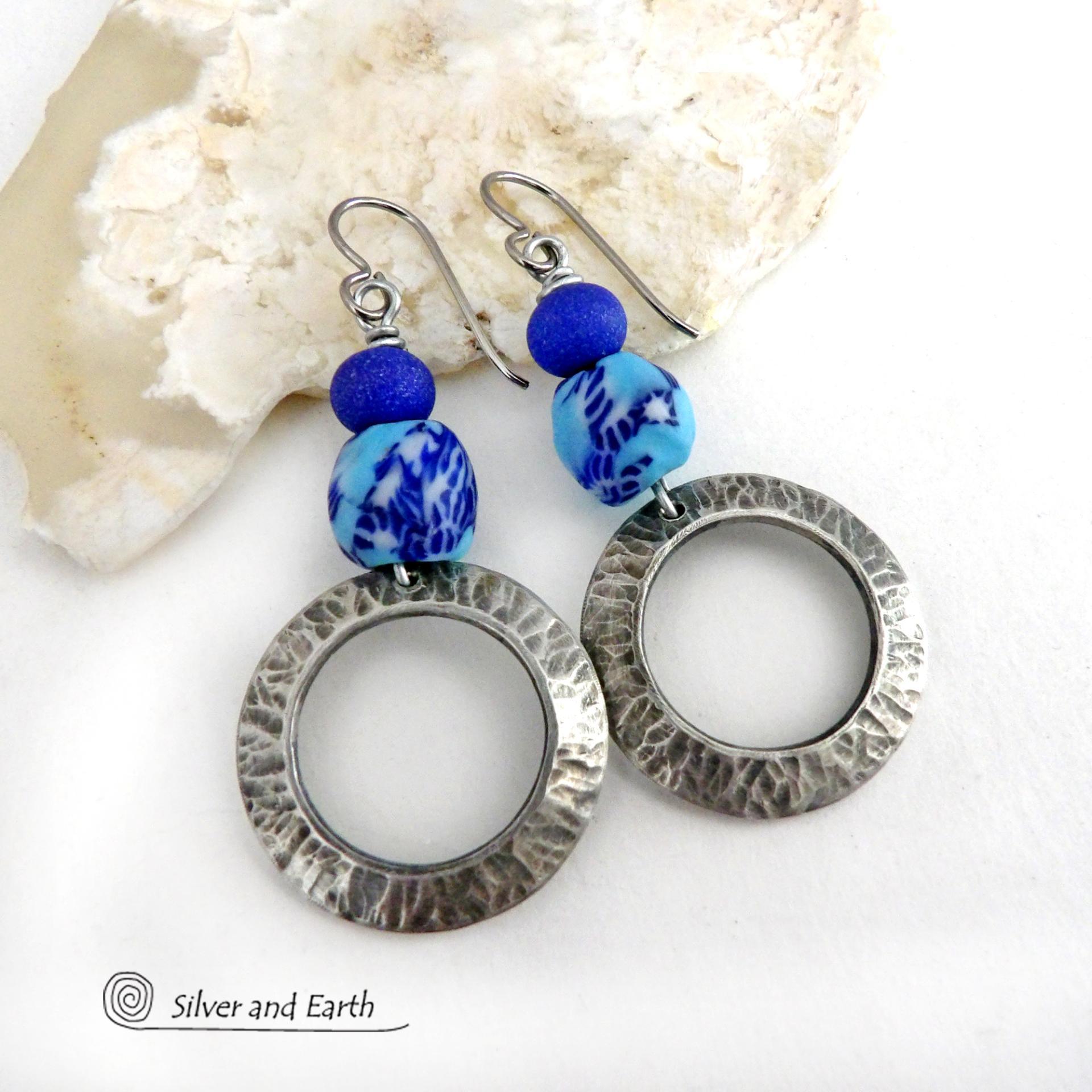 These handcrafted silver pewter hoop earrings have a hammered texture and feature blue African glass beads accented with bright blue glass beads. Vibrant and colorful, they'll add a touch of boho chic flair to your wardrobe. The African beads are handcrafted by artisans in Ghana from recycled glass by a traditional process passed down thru many generations. Handmade in the USA by Silver and Earth Jewelry. MEASUREMENTS: Total length: approximately 2-1/8" from top of silver niobium (hypoallergenic) ear wire