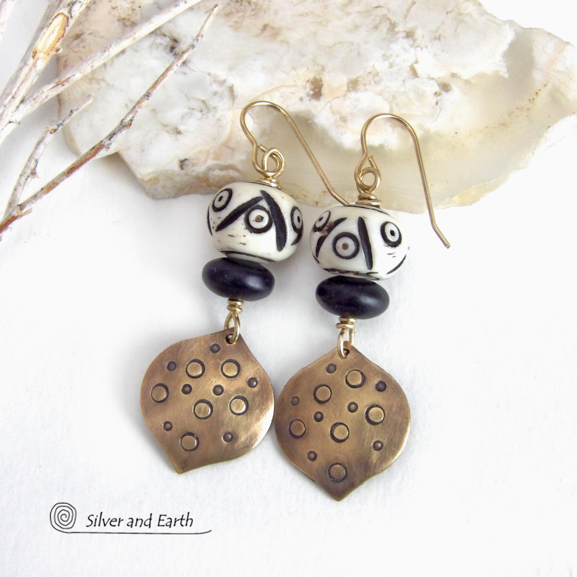 These handcrafted gold brass earrings have an ethnic, boho tribal vibe that makes a unique bold statement. They feature brass drops with a hand stamped texture accented with African carved bone beads with a bold pattern of dots and lines and matte black glass beads. Perfect for women that love unique handmade jewelry. Handmade in the USA by Silver and Earth Jewelry.