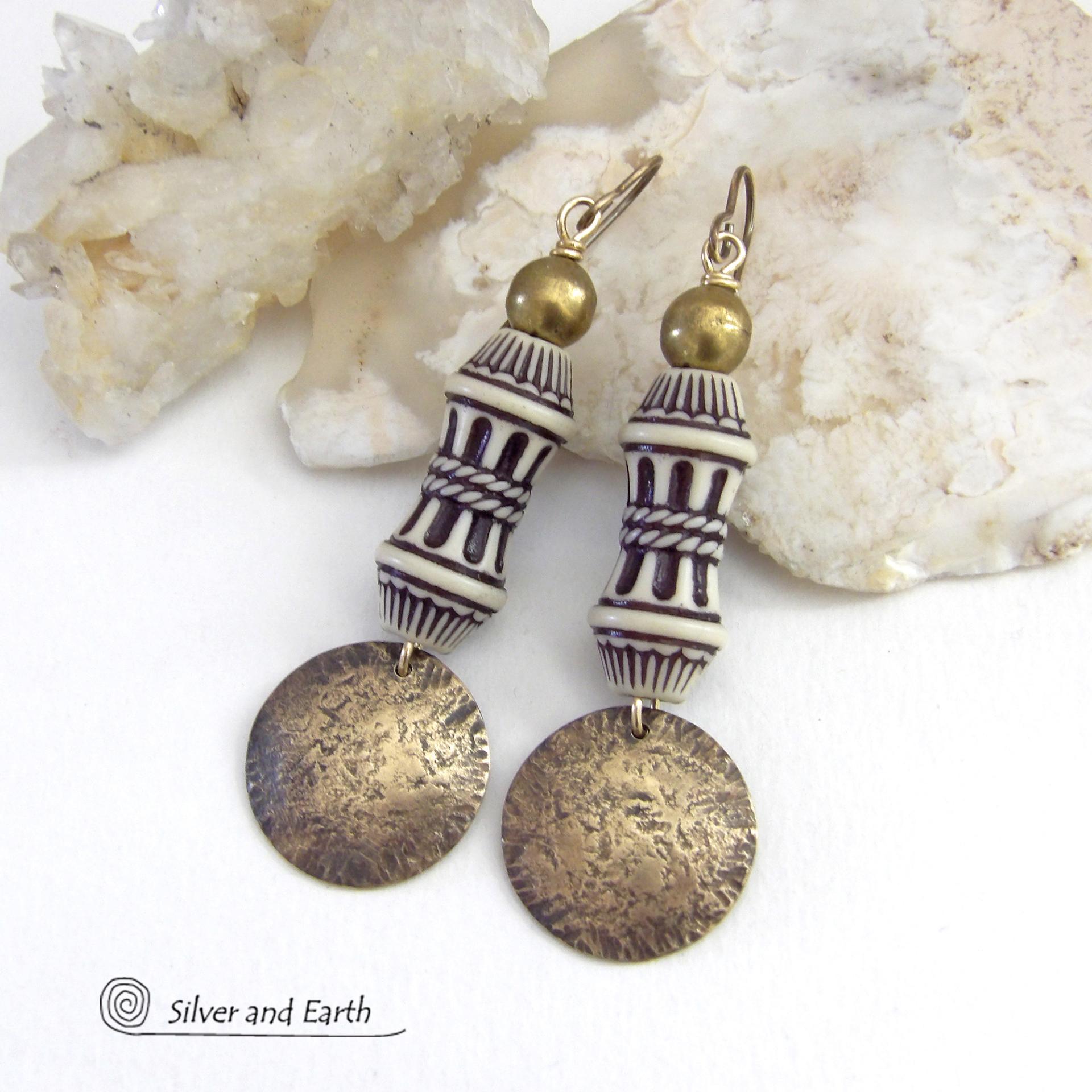 Bold and unique, these handcrafted earrings have an ethnic African tribal vibe. They feature gold brass dangles with a hammered rustic texture accented with exotic African beads with an intricate brown and white carved pattern topped off with gold brass beads. Unique and fun to wear - they'll make a bold, striking statement. Perfect for women that love to wear one-of-a-kind artisan handcrafted jewelry. Handmade in the USA by Silver and Earth Jewelry. 