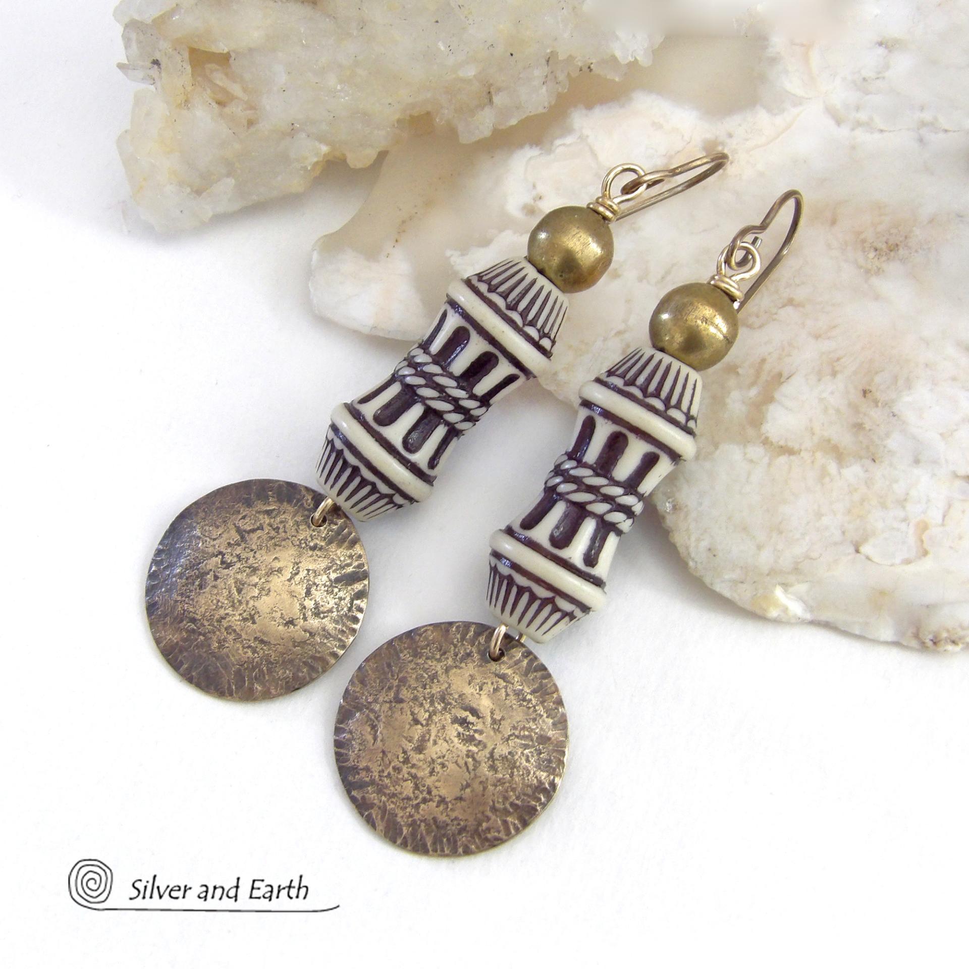 Bold and unique, these handcrafted earrings have an ethnic African tribal vibe. They feature gold brass dangles with a hammered rustic texture accented with exotic African beads with an intricate brown and white carved pattern topped off with gold brass beads. Unique and fun to wear - they'll make a bold, striking statement. Perfect for women that love to wear one-of-a-kind artisan handcrafted jewelry. Handmade in the USA by Silver and Earth Jewelry. 