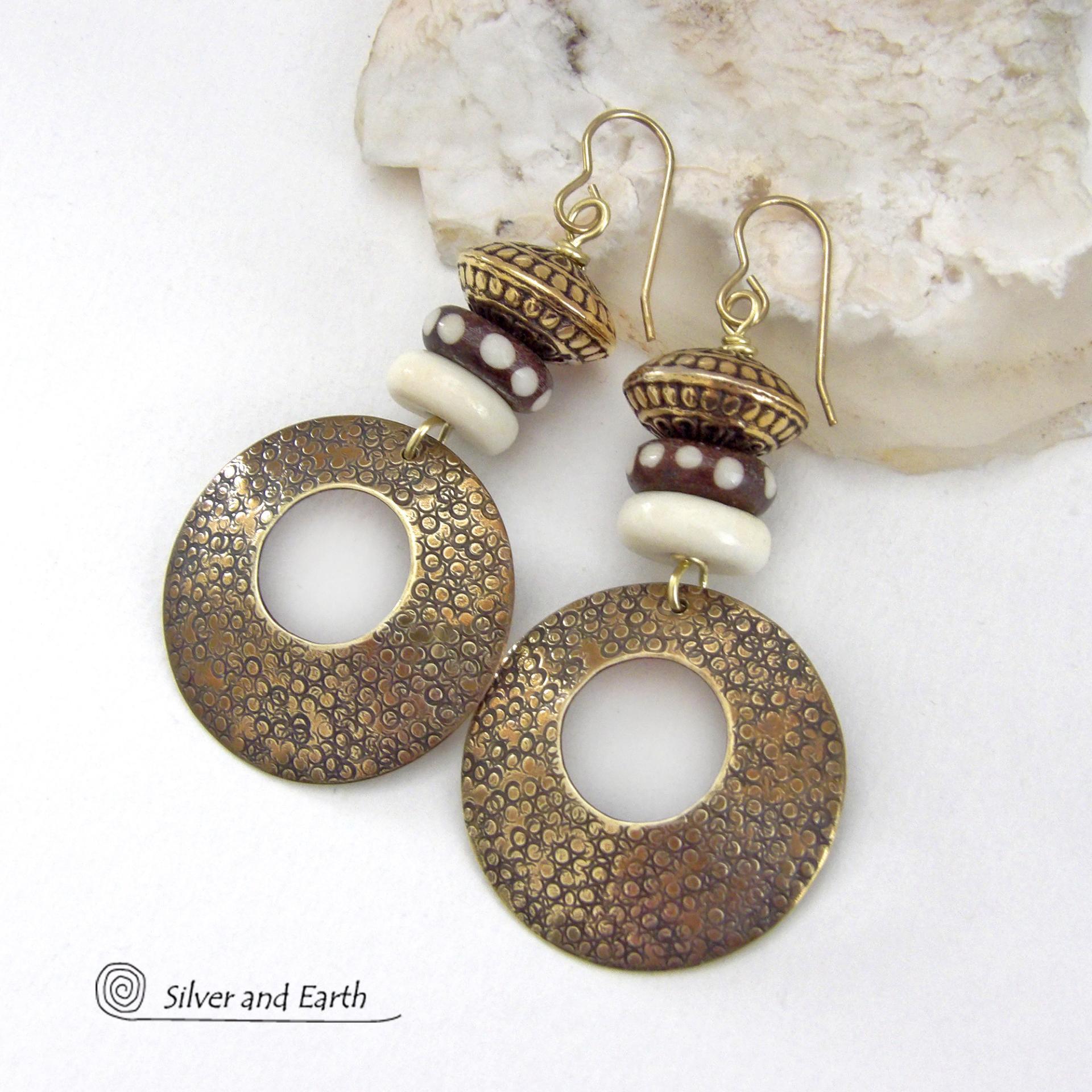 Big and bold, these handcrafted gold brass hoop earrings have a hand stamped texture and are accented with African batik bone dark brown beads with a dotted pattern, off-white bone beads and textured gold brass beads. They have an exotic ethnic and boho chic vibe that makes a striking, unique statement. Handmade in the USA by Silver and Earth Jewelry.