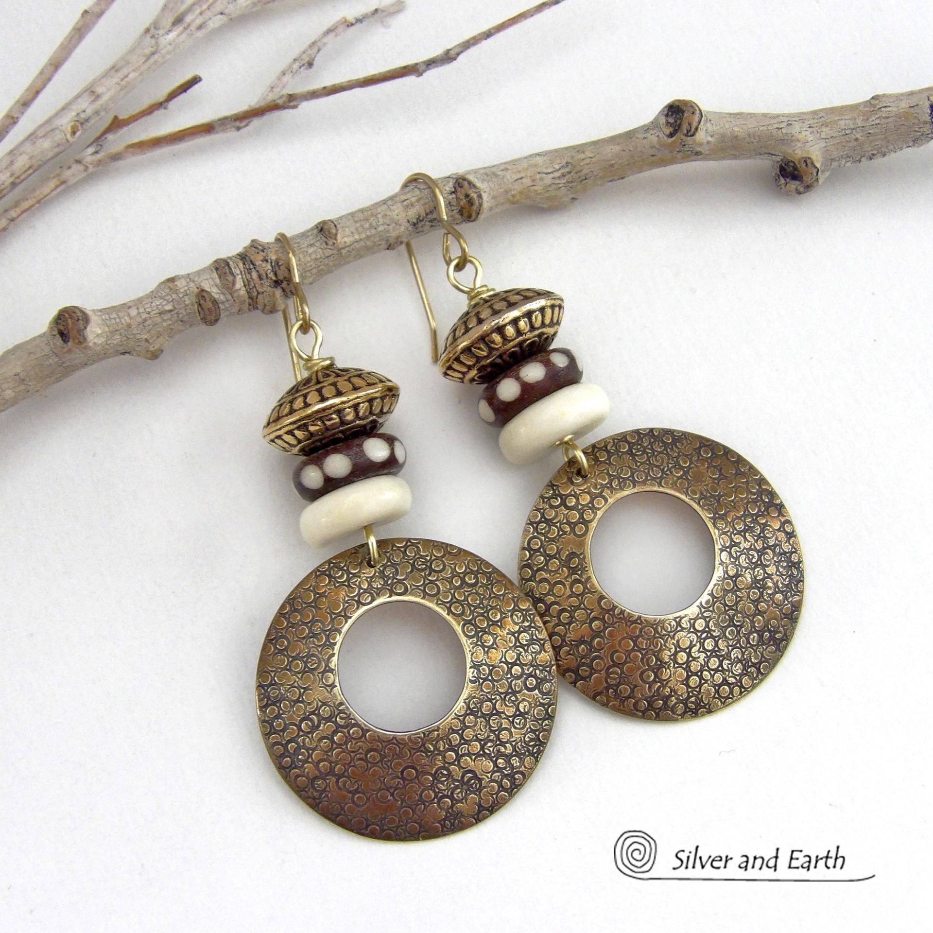 Big and bold, these handcrafted gold brass hoop earrings have a hand stamped texture and are accented with African batik bone dark brown beads with a dotted pattern, off-white bone beads and textured gold brass beads. They have an exotic ethnic and boho chic vibe that makes a striking, unique statement. Handmade in the USA by Silver and Earth Jewelry.