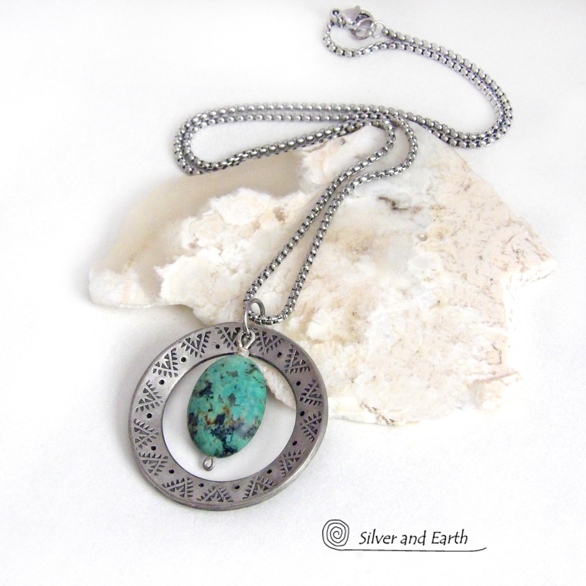 This handcrafted pendant necklace features a natural African turquoise gemstone dangling in front of a silver tone pewter circle with a hand stamped texture and oxidized finish. Unique and one of a kind, it has an earthy organic style with southwestern flair. Coordinating earrings sold separately.