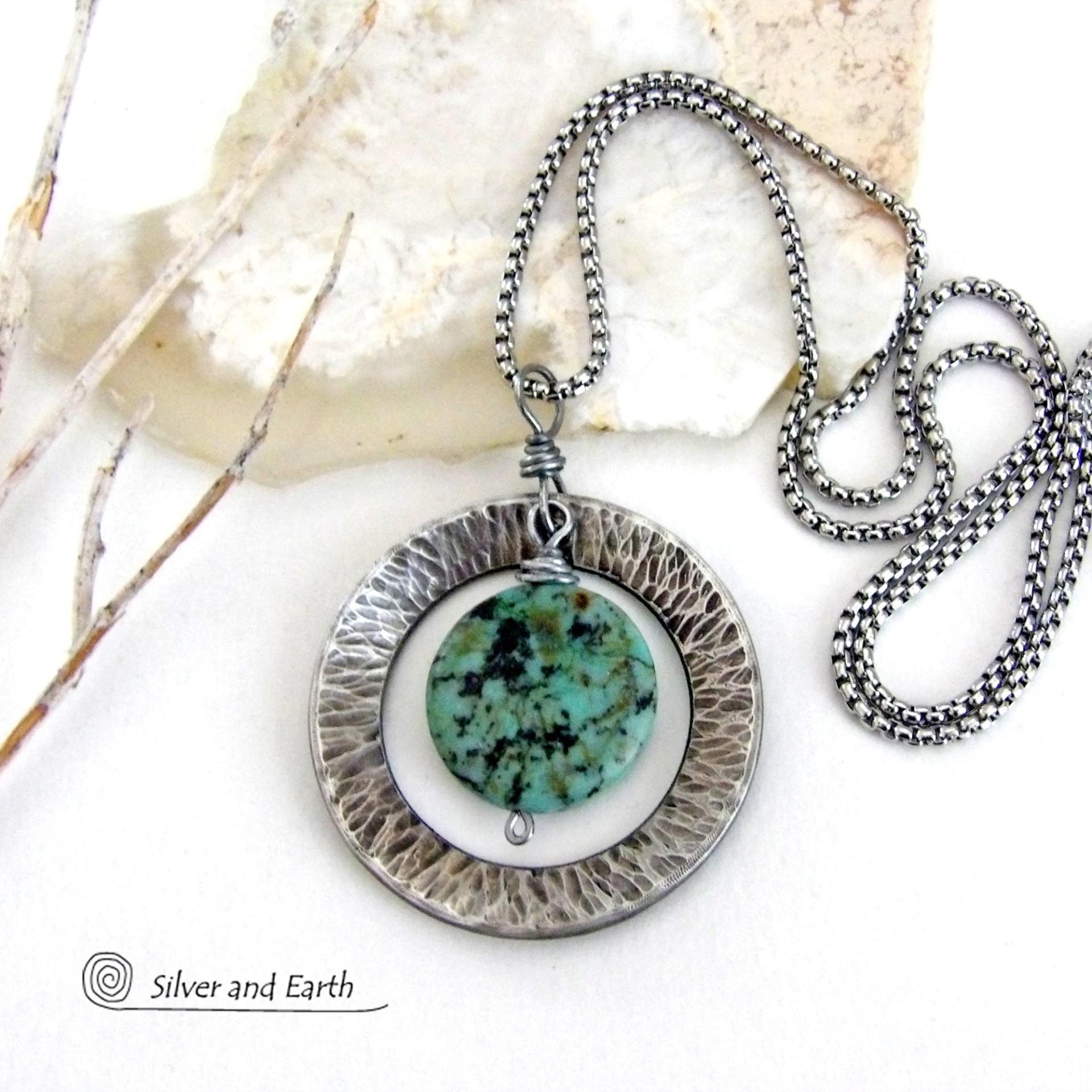 This handcrafted pendant necklace features a natural coin-shaped African turquoise gemstone framed against a hammered and oxidized silver tone pewter circle. It has a modern earthy organic style that coordinates well with all wardrobe types. The design is versatile and can be worn by either a man or woman. It will make a great gift for anyone that loves natural stone jewelry. Handmade in the USA by Silver and Earth Jewelry. 