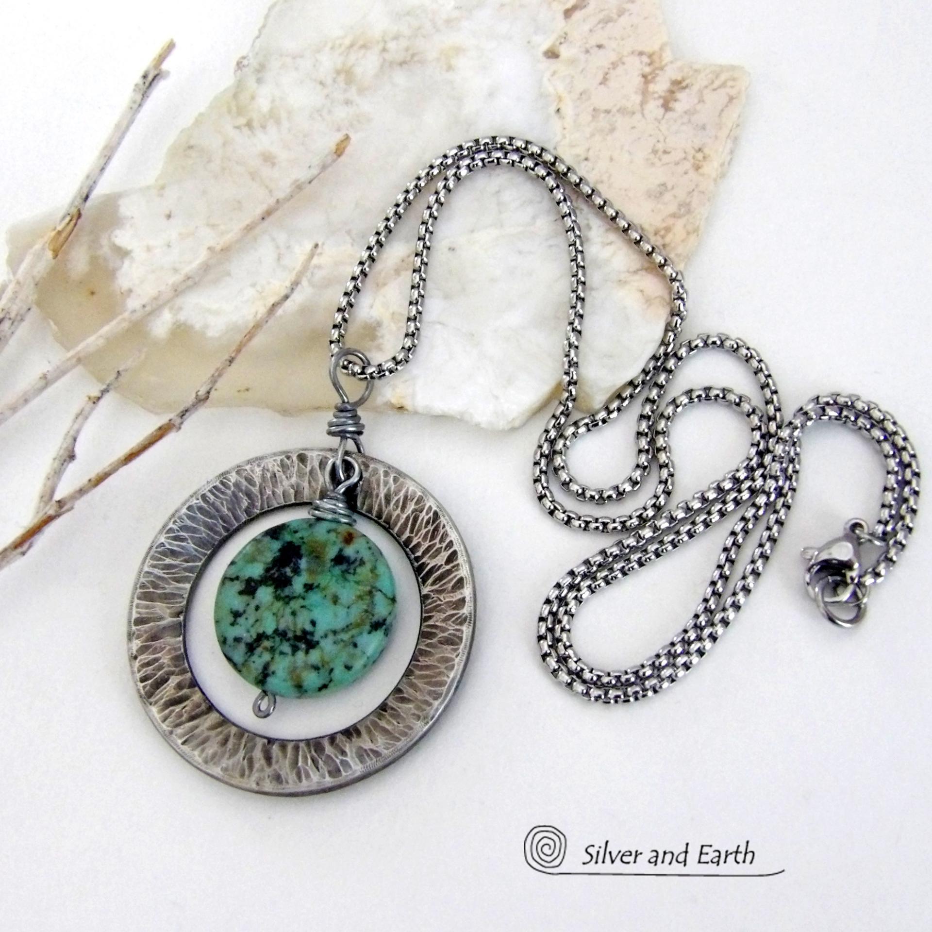 This handcrafted pendant necklace features a natural coin-shaped African turquoise gemstone framed against a hammered and oxidized silver tone pewter circle. It has a modern earthy organic style that coordinates well with all wardrobe types. The design is versatile and can be worn by either a man or woman. It will make a great gift for anyone that loves natural stone jewelry. Handmade in the USA by Silver and Earth Jewelry. 