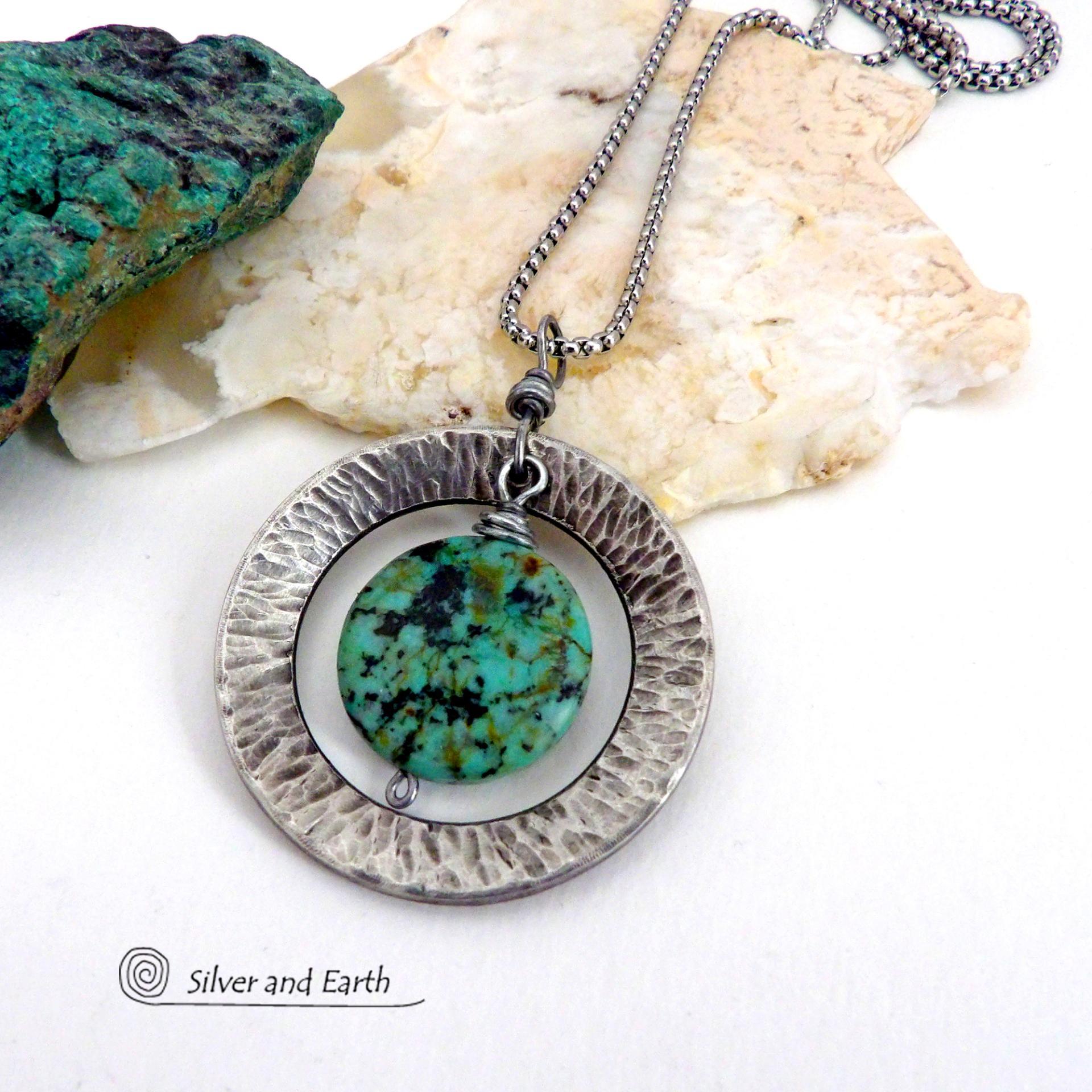 This handcrafted pendant necklace features a natural coin-shaped African turquoise gemstone framed against a hammered and oxidized silver tone pewter circle. It has a modern earthy organic style that coordinates well with all wardrobe types. The design is versatile and can be worn by either a man or woman. It will make a great gift for anyone that loves natural stone jewelry. Handmade in the USA by Silver and Earth Jewelry. 
